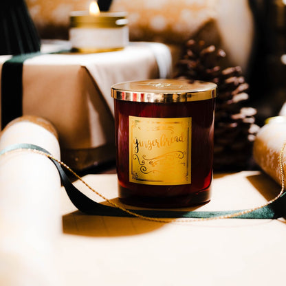 A red 16oz soy christmas candle with a gold lid and a gold label named "gingerbread" sitting on wrapped christmas presents.