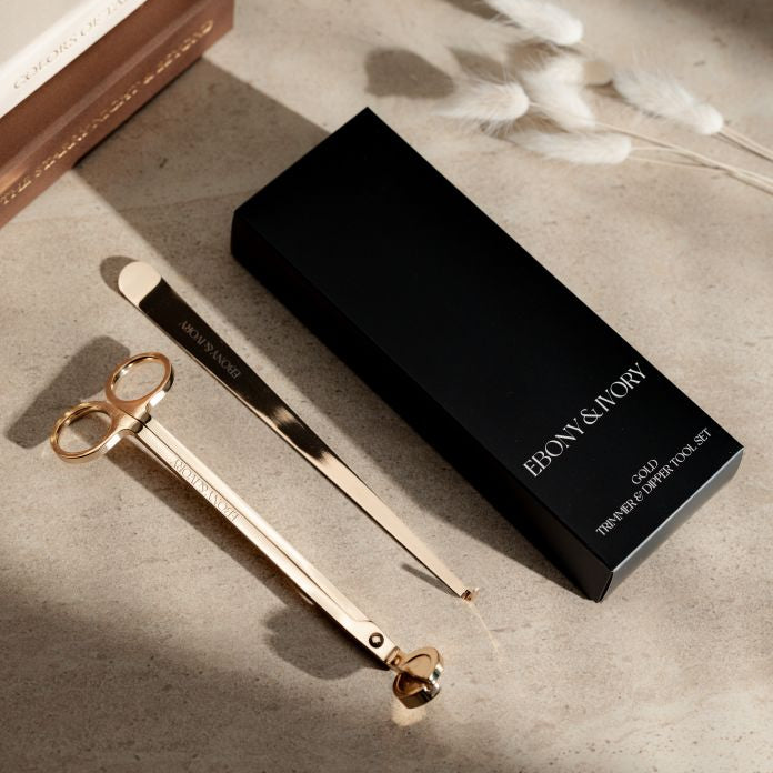 A black box for a set of 2 candle tools. The tools are a gold wick trimmer and a gold wick dipper with white Ebony & Ivory logos
