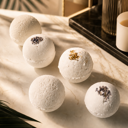 White bath bombs with decorative elements on a marble surface with a mirror and candle in the background.