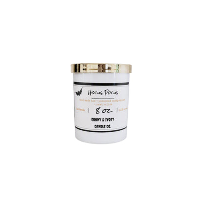 A white 8oz soy wax candle with a gold lid and a white label named "hocus pocus"