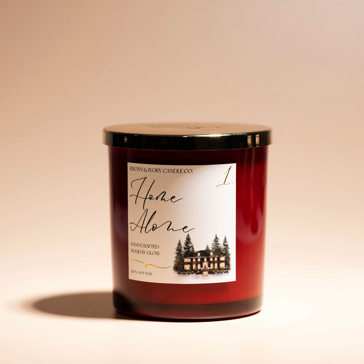 A red 16oz soy christmas candle with a gold lid and a white label named "home alone 1" on a beige background