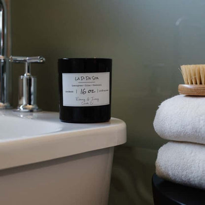 A black jar 16oz soy candle with a white label named La Di Da Spa, on the edge of a white bath tub, made by Ebony & Ivory Candle Co in Lethbridge, Alberta, Canada