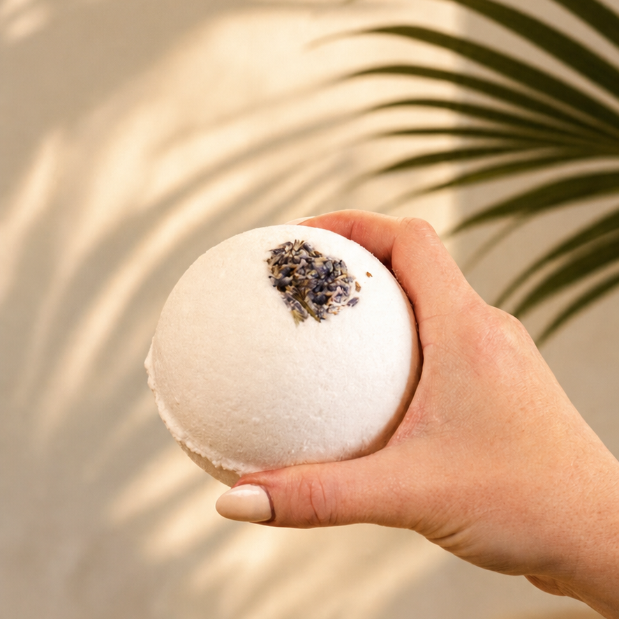 Hand holding a white bath bomb with a decorative top against a neutral background