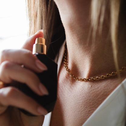 Person holding a perfume bottle with a gold necklace. long lasting perfume for women jasmine cherry scent.