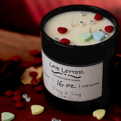 Candle with heart-shaped candies on top and a label reading 'Love Letter' on a wooden surface. Soy candle for valentines day.