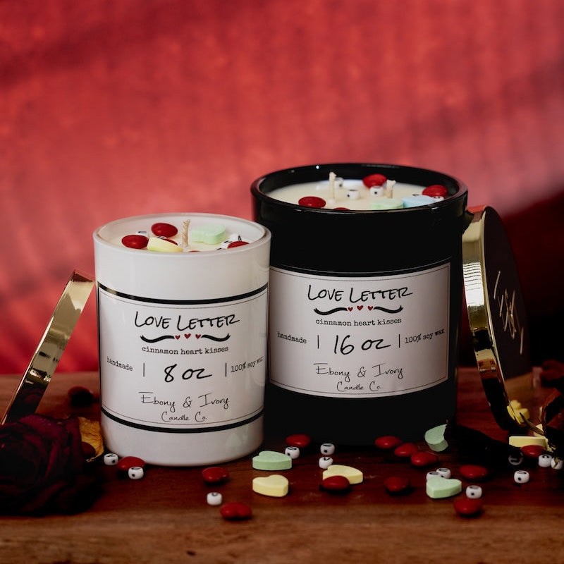 Two candles with decorative elements on a wooden surface against a red background. valentines day candles made from soy wax in Canada for valentine's day. 