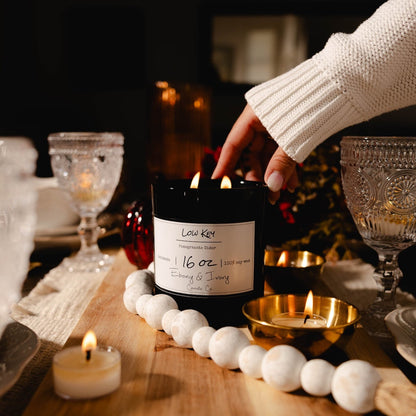 Person lighting a candle on a table with decorative items. Beautiful table setting with black vessel soy candle.