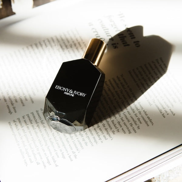 long lasting perfume for women jasmine cherry scent. black perfume bottle sitting in decor magazine book with a gold lid and heart shadow.