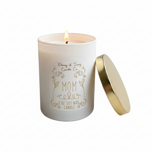 A white 8oz soy candle with a gold lid and a white label with gold lettering that reads "Mom" made by ebony & ivory candle co in lethbridge alberta canada