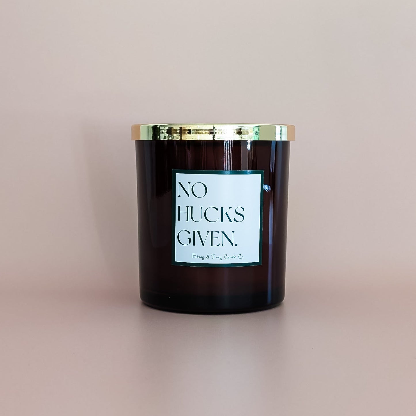 An amber jar 16oz soy candle with a gold lid and a white label named No Hucks Given, on an ivory background, made by Ebony & Ivory Candle Co in Lethbridge, Alberta, Canada