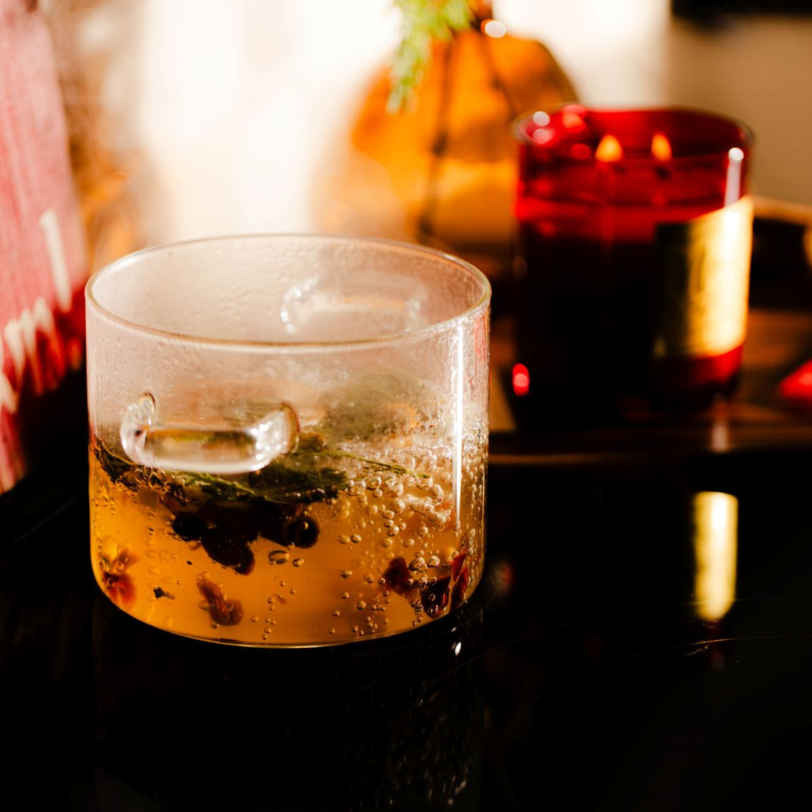 A clear glass simmer pot on a stove with a red christmas candle burning in the background.