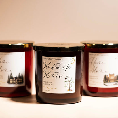three 16oz soy christmas candles on a beige background with gold lids and white labels.