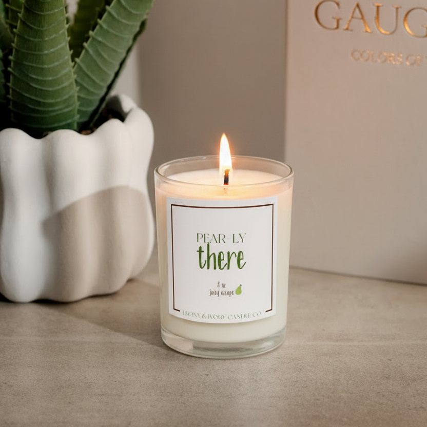 a clear glass 8oz soy candle sitting on table with the wick lit. The candle has a white label and is named "Pear-ly There"
