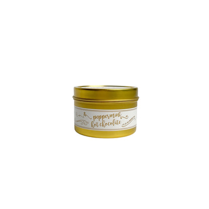 A gold 4oz soy christmas candle with a white and gold label named "peppermint hot chocolate"