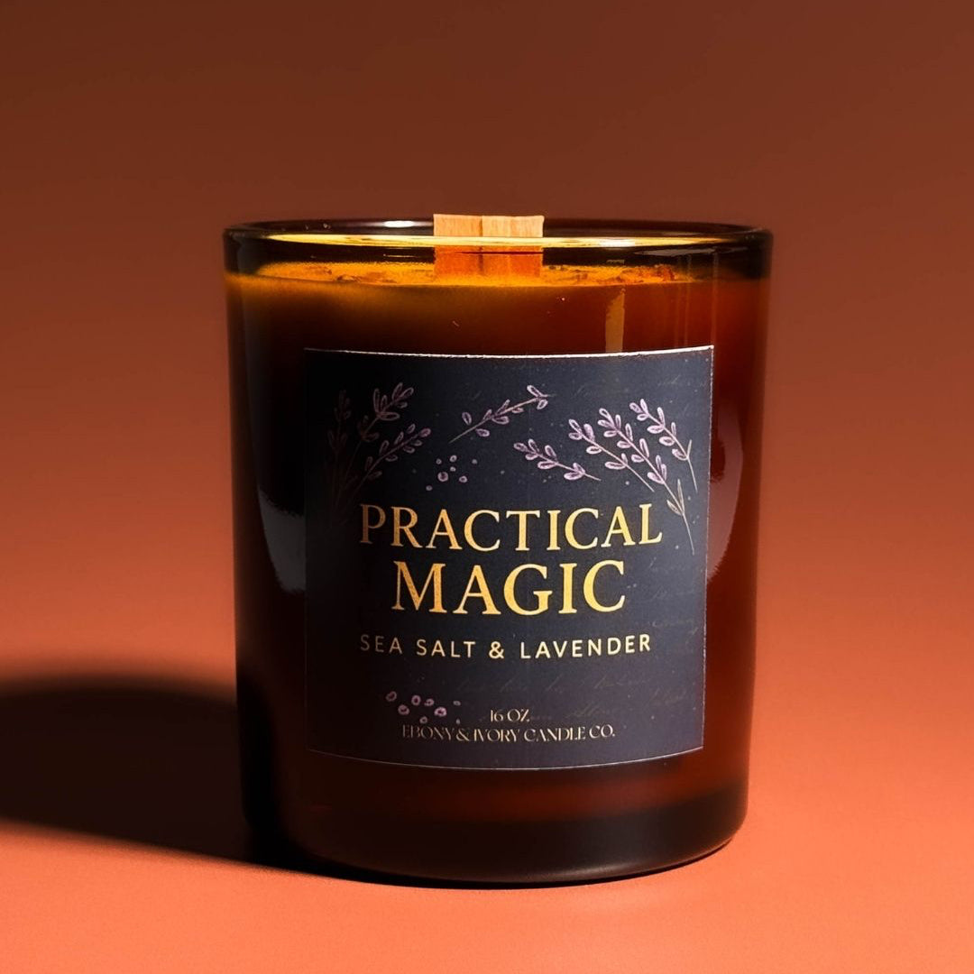 An amber jar 16oz soy wax candle with a wood wick, a gold lid, and an indigo label named "practical magic" on an amber background