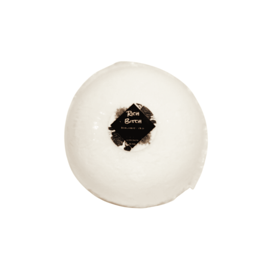 A white bath bomb with a round sticker label named Rich Bitch, on a white background, made by Ebony & Ivory Candle co in Lethbridge, Alberta, Canada
