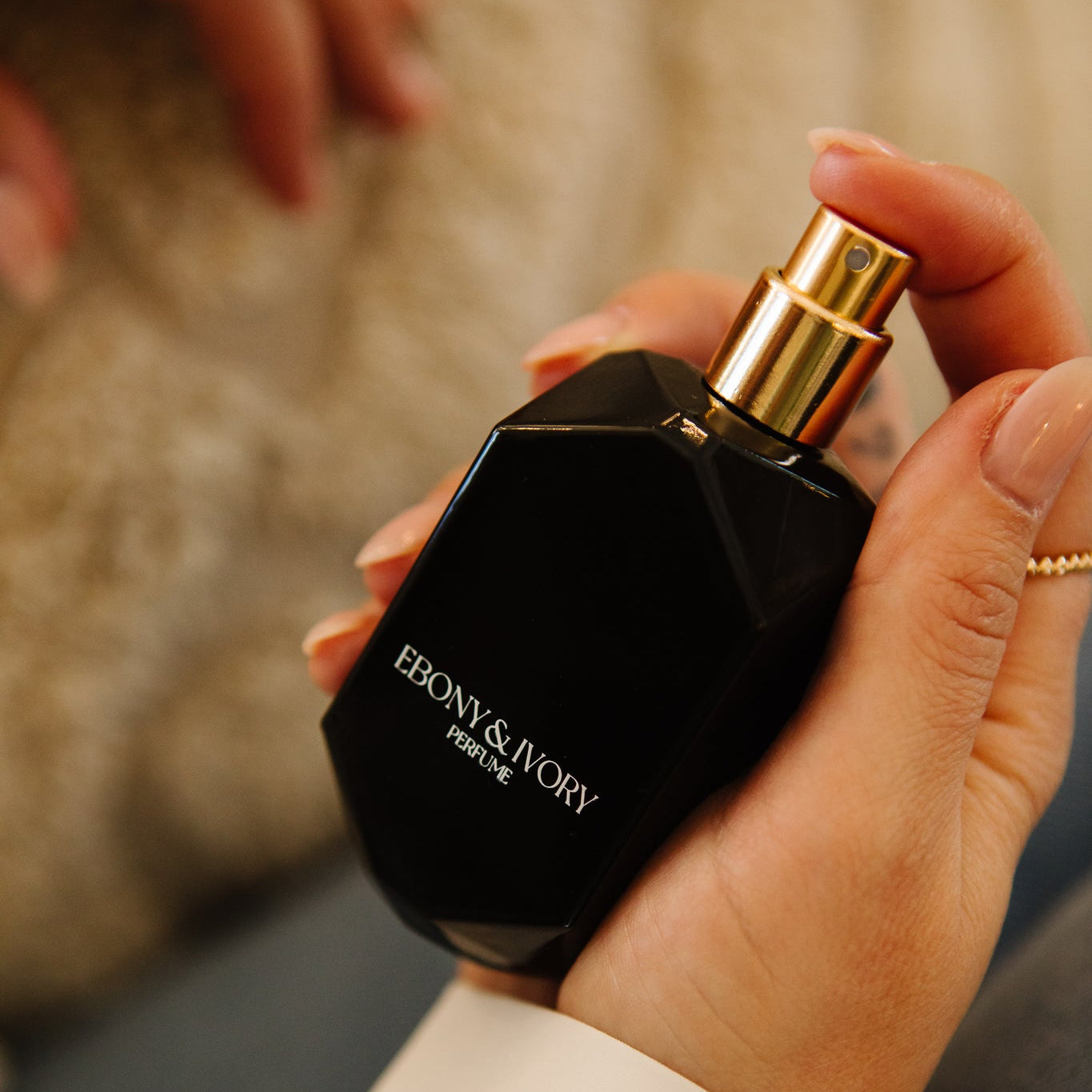 Hand holding a black perfume bottle with gold cap, featuring the brand 'Ebony & Ivory'.