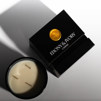 A top down view of a black 18oz jar coconut soy candle with a white Ebony & Ivory on the front next to a black candle box with a gold label named sinner, on a white background, made by Ebony & Ivory Candle Co in Lethbridge, Alberta, Canada