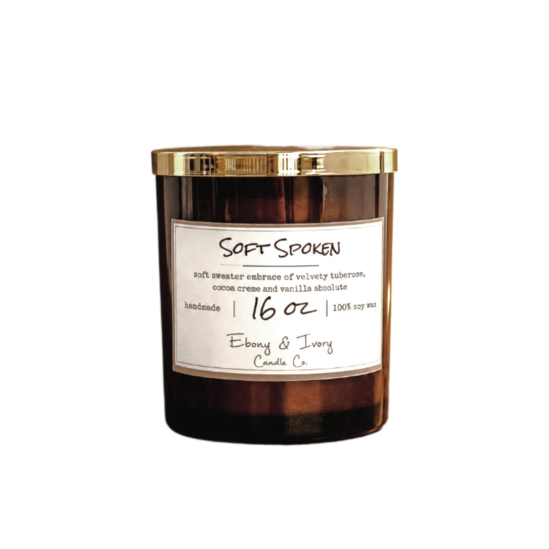 A 16oz Amber glass jar soy candle with a gold lid and a white label named "soft spoken"
