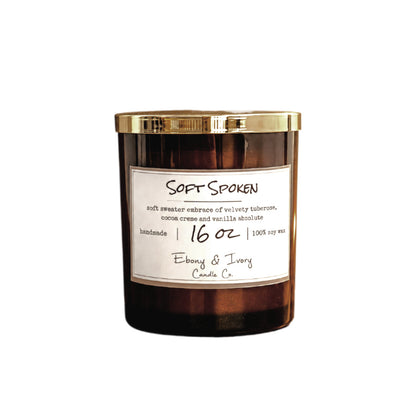A 16oz Amber glass jar soy candle with a gold lid and a white label named "soft spoken"