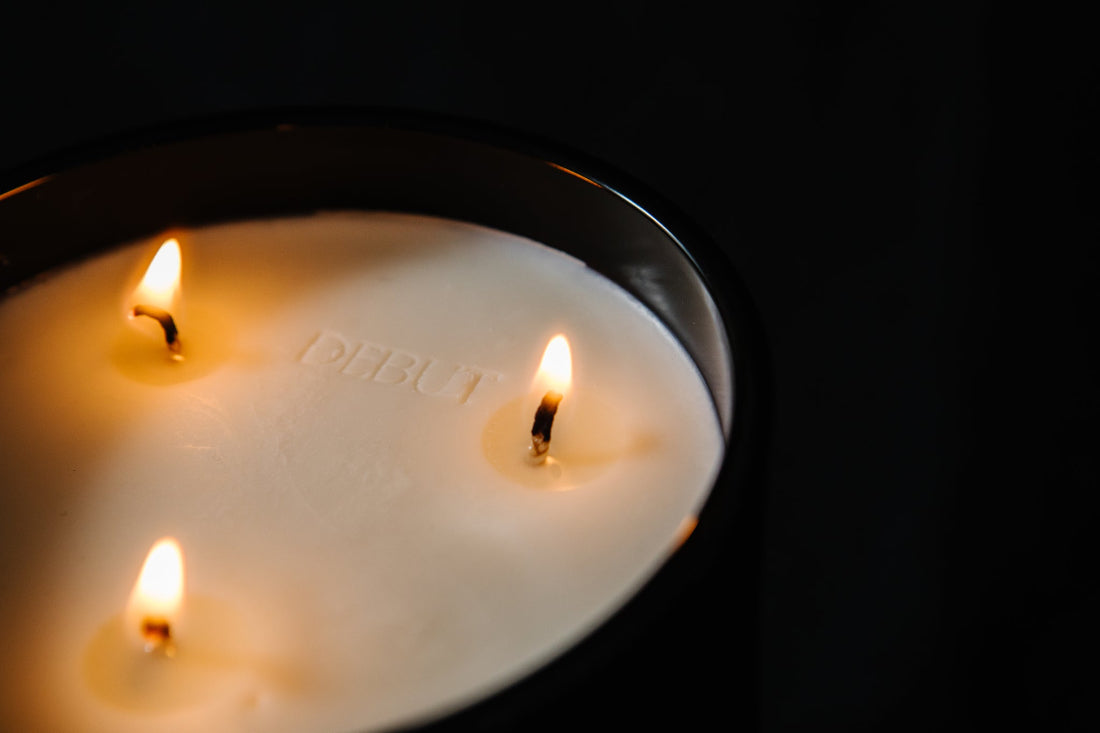 Three lit candles in a glass container with 'Debut' branding on a black background