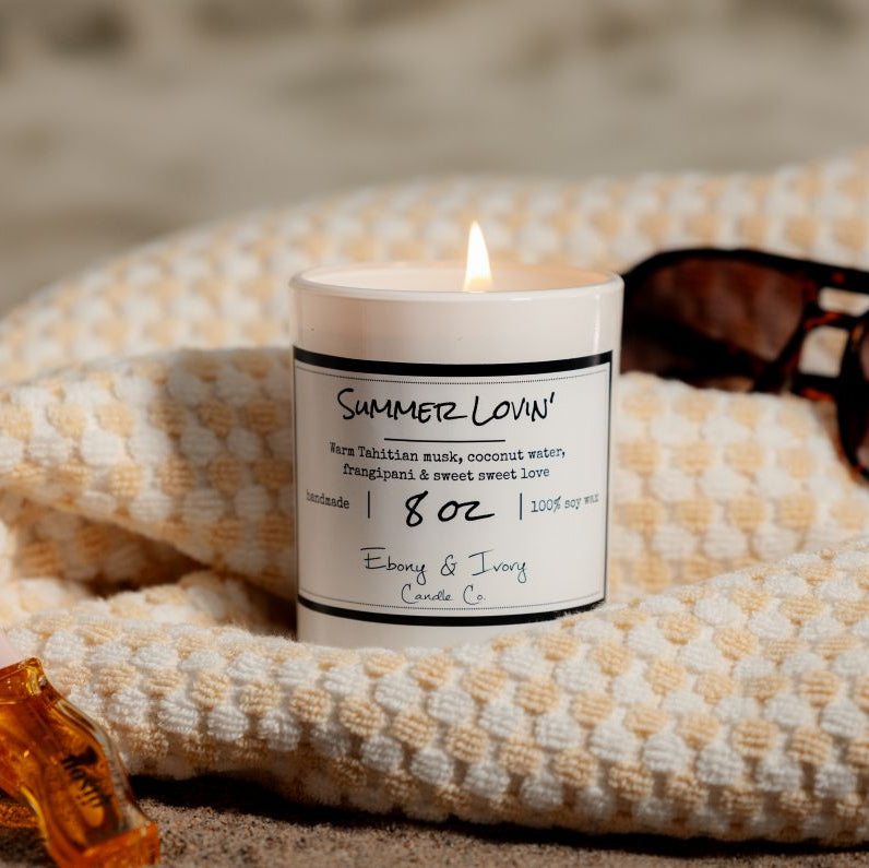 a white 8oz soy candle labelled Summer Lovin sitting on a beach towel with sunglasses. Made in Lethbridge Alberta Canada