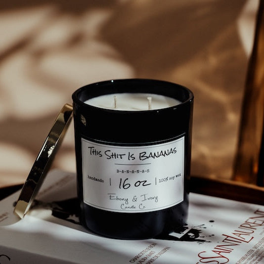 Two candles with labels on a Yves Saint Laurent box against a blurred background.  Banana scented soy candle Canada.