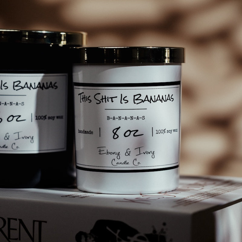 Two candles with labels on a Yves Saint Laurent box against a blurred background. Yves saint Laurent book decor with Canadas soy candle. Banana scented soy candle Canada.