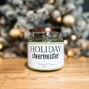 Clear, sixteen ounce, evergreen trees, citrus, clove, and nutemeg scented, green soy wax candle with a white label and bronze lid