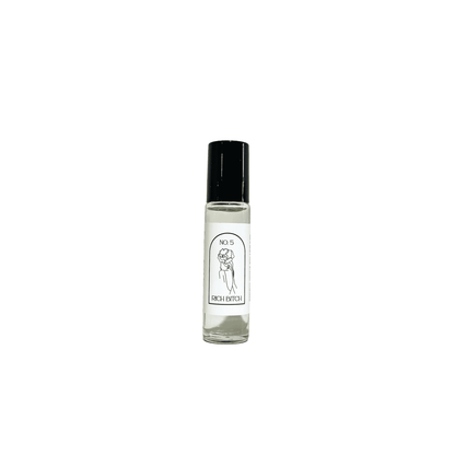 A clear 10ml argan oil roll on, with a black lid and a white label named Rich Bitch, on a white background, made by Ebony & Ivory Candle Co in Lethbridge, Alberta, Canada