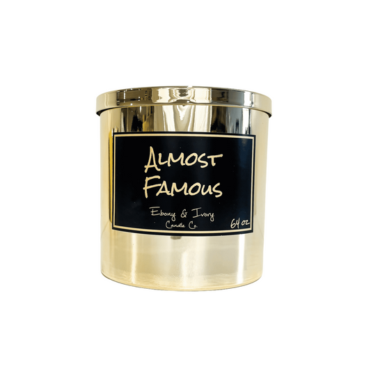 gold sixty four ounce, citrus, jasmine, and woodsy scented soy wax candle with a gold lid and a black label that reads Almost Famous