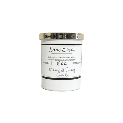 White eight ounce, apple, cinnamon, and clove scented soy wax candle with a gold lid and a white label that reads Apple Cider