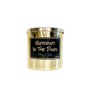 Gold, sixty four, blue spruce and huckleberry scented soy wax candle with a gold lid and a black label that reads Berried in the Pines