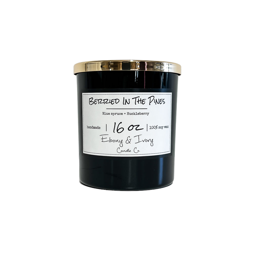 Black, sixteen ounces, blue spruce and huckleberry scented soy wax candle with a gold lid and a white label that reads Berried in the Pines