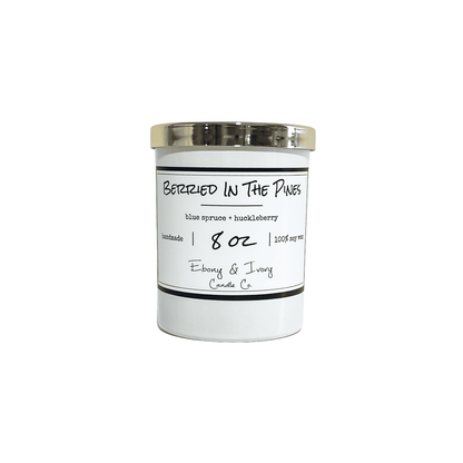 A white 8oz jar soy candle with a gold lid and a white label named Berried in the Pines, on a white background, made by Ebony & Ivory Candle Co in Lethbridge, Alberta, Canada