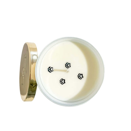 A top down view of a white 8oz soy candle with four black paw print glitters on top to look like a pet walking across. Made by Ebony & Ivory Candle co in Lethbridge Alberta Canada