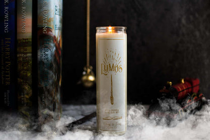 Tall 16oz clear glass jar soy candle with a green label named Lumos, on a marble table with harry potter books, a wand, and the hogwarts train behind it, with smoke billowing around. apart of the wizarding candle collection made by Ebony & Ivory Candle Co in Lethbridge, Alberta, Canada