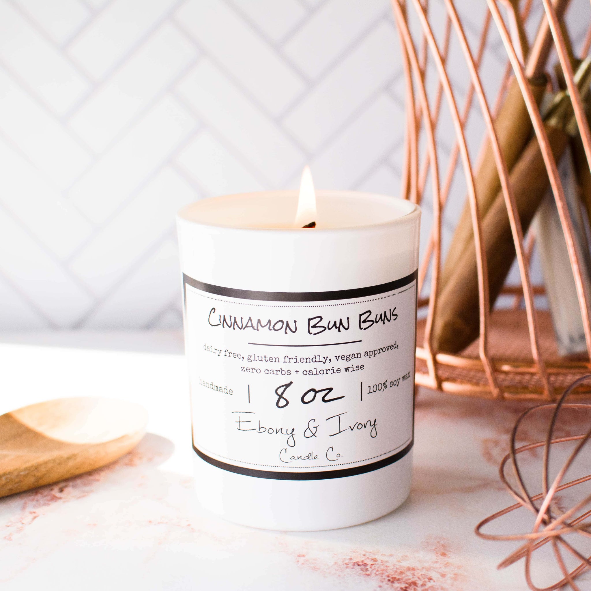White, eight ounces, cinnamon roll scented soy wax candle with a gold lid and a white label that reads Cinnamon Bun Buns