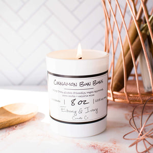 White, eight ounces, cinnamon roll scented soy wax candle with a gold lid and a white label that reads Cinnamon Bun Buns