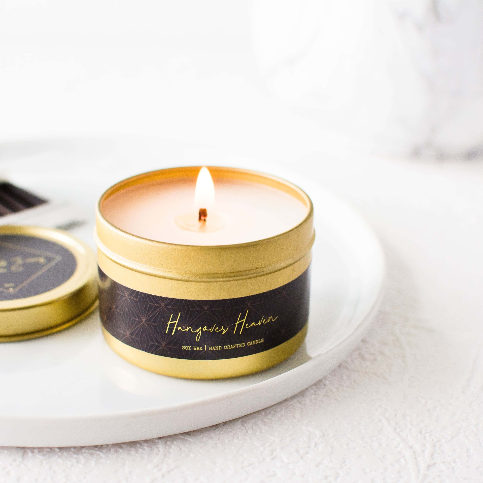 A gold 4oz tin soy candle with a gold lid and a black label named Hangover Heaven, on a white tray, made by Ebony & Ivory Candle Co in Lethbridge, Alberta, Canada