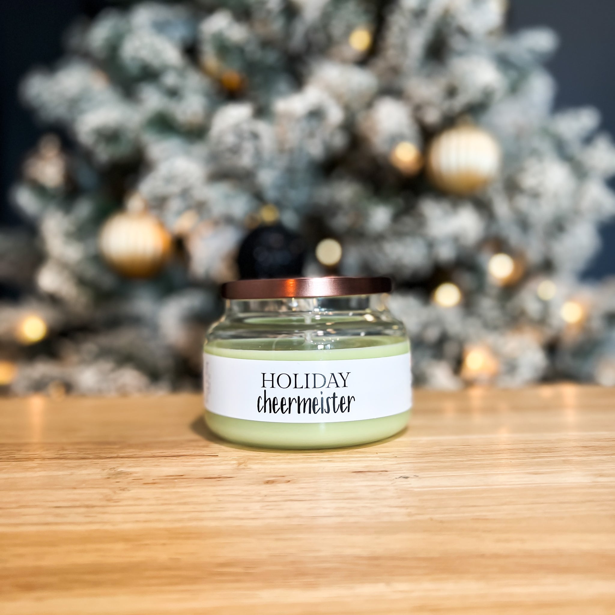 Clear, eight ounce, evergreen trees, citrus, clove, and nutemeg scented, green soy wax candle with a white label and bronze lid