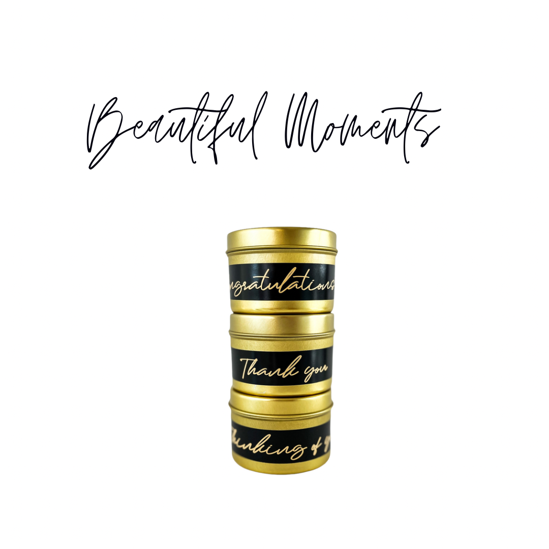 Stack of three gold, 4 ounce, pink salt and water lily scented soy wax candles with gold lids and black labels. At the top there is black text that reads Beautiful Moments