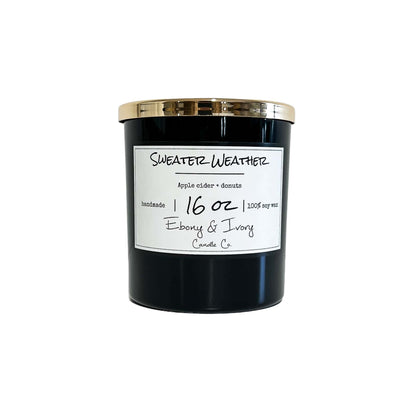 A black jar 16oz soy candle with a gold lid and a white label named Sweater Weather, on a white background, made by Ebony & Ivory Candle Co in Lethbridge, Alberta, Canada