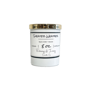 White, eight ounce, apple cider and donuts scented soy wax candle with a white label that reads Sweater Weather