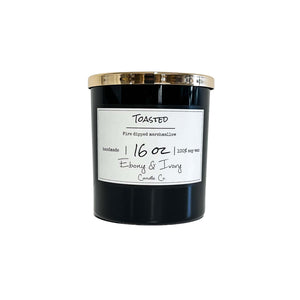 Black, sixteen ounce, marshmallow, vanilla, and woodsy scented soy wax candle with a gold lid and a white label that reads Toasted